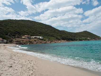 A wide sandy beach meets the clear blue sea with green hills and houses in the background, ajaccio,