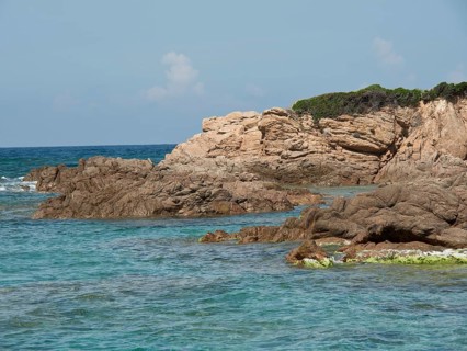 Rough rocky coast lapped by turquoise sea under a slightly cloudy sky, ajaccio, corsica, france