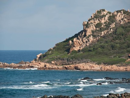 Rocky cliffs with plants and the sea with waves under a blue sky, ajaccio, corsica, france
