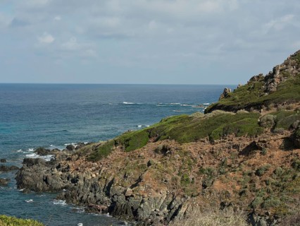 Rocky coast with dense greenery and calm sea, cloudy blue sky over the sea, ajaccio, corsica,