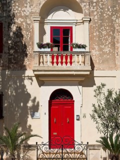 Charming building with bright red windows and doors and a small balcony with flowers, mdina,