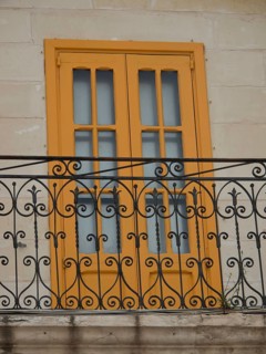 Yellow shutters with an ornate wrought-iron balcony, marsaxlokk, mediterranean sea, malta