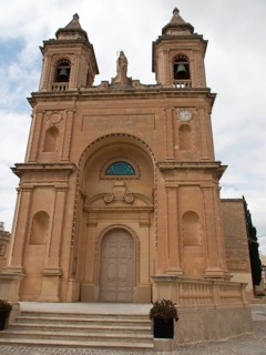An imposing sandstone-style church with two towers and a detailed façade, marsaxlokk, mediterranean