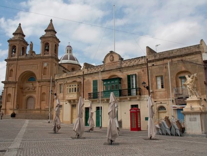 A historic square with a large church and surrounding buildings under a cloudy sky, marsaxlokk,