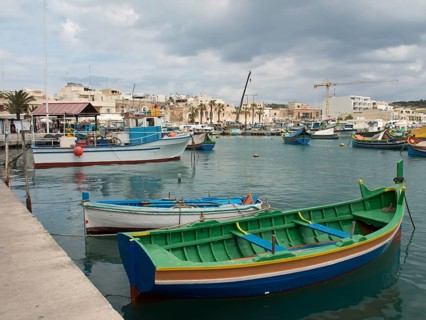 Colourful boats in the harbour overlooking a small town, under a cloudy sky, marsaxlokk,