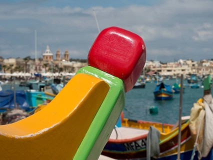 A colourful detail of a boat with a busy harbour and town in the background, marsaxlokk,