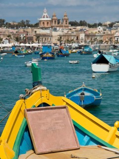View from the bow of a boat of a harbour town with several boats in the water, marsaxlokk,