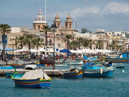 Lively harbour with colourful boats, palm trees and historic churches in the background,