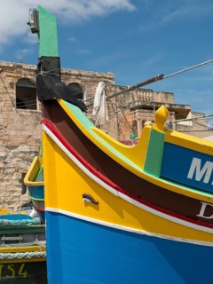 Colourful traditional boats in the harbour with historic stone walls in the background, marsaxlokk,