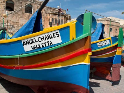Multicoloured fishing boats parked in front of a historic building in Valletta, Malta, marsaxlokk,