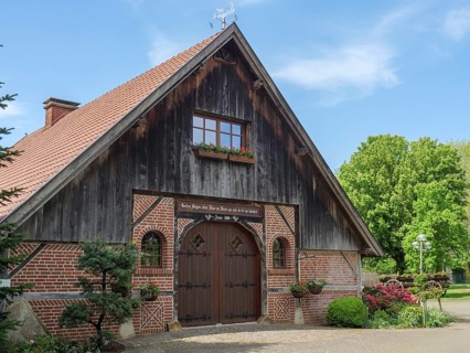 Rustic barn made of wood and brick with flowers and plants in the foreground under a blue sky,