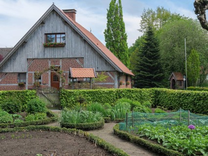 A half-timbered house with a large garden, including vegetable patches and surrounded by green