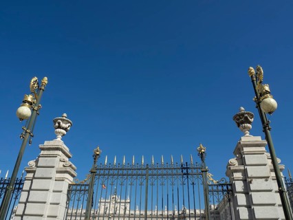 Black, wrought-iron fence with golden decorations encloses a historic building under a clear sky,