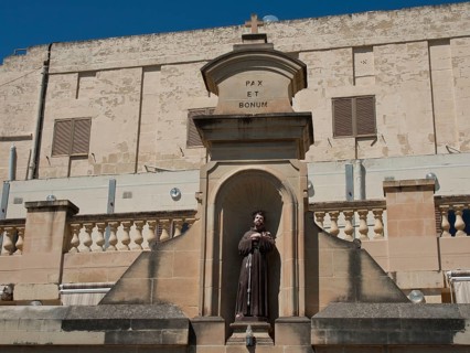 Statue of a monk in a stone niche in front of a historic building, stone wall with inscription Pax