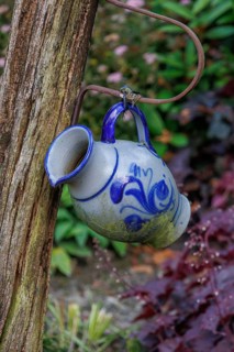 Close-up of a blue and white decorative jug hanging from a wooden post in a flowery garden, Borken,