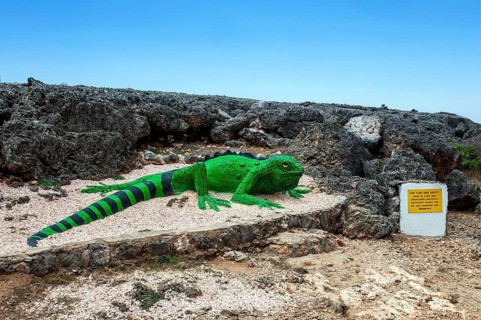 Sculpture figure of artificial oversized iguana in front of rocky terrain at the beginning of Boka