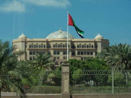 An imposing palace with a waving flag and surrounded by palm trees, abu dhabi, united arab emirates
