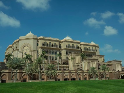 Magnificent palace with palm trees and green lawn under a clear sky, abu dhabi, united arab