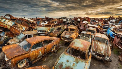 A large pile of rusty cars in a junkyard under a colourful sky at sunset, symbol photo, AI
