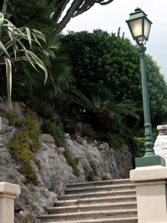 A steep stone staircase leads past densely overgrown plants and a green street lamp, monte carlo,
