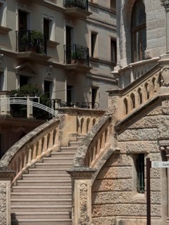 Stone staircase with ornate balustrade in front of historic buildings with balconies and ornate
