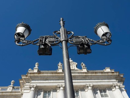 Close-up of a wrought-iron street lamp in front of a historic building under a blue sky, Madrid,