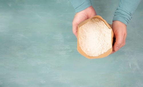 Baker holds paper bag with white wheat flour, baking ingredient for bread, pizza or pastry