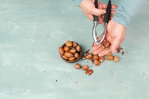 Crack nuts with a nutcracker, mix variety of almonds, hazelnuts and pecan nuts, healthy food and