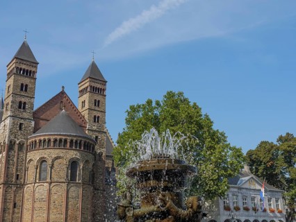 A fountain bubbles in front of a historic church building with two towers, Maastricht, limburg,