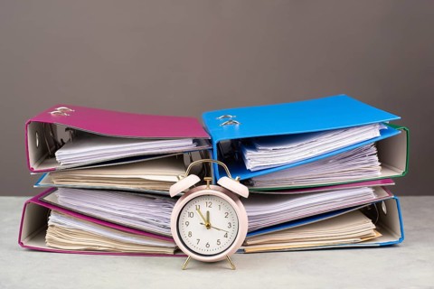 Alarm clock standing next to pile of file folders, burnout, stress and overworked, pressure at