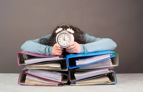 Exhausted tired woman with alarm clock sleeping on a pile of file folders, burnout, stress and