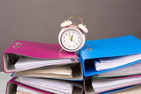 Alarm clock standing on pile of file folders, burnout, stress and overworked, pressure at work,