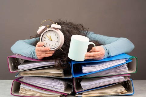 Exhausted tired woman with coffee and alarm clock, pile of file folders, burnout, stress and