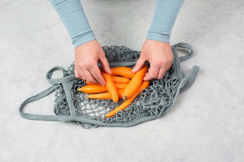 Unpack fresh carrots from a reusable grocery mesh bag, vegetables from the market, healthy food and