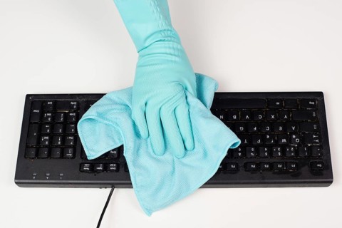 Cleaning computer keyboard in office with a wet wipe rag, dusty and dirty electronic, housework
