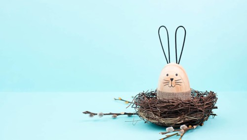Easter bunny or rabbit sitting in a bird nest, willow branches, wooden egg, spring holiday, brown