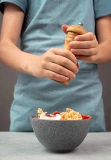Putting pepper in a pasta salad, sliced mushroom, tomato, red pepper pieces and tuna, healthy food
