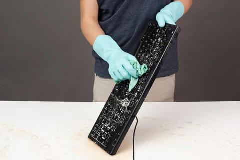 Cleaning computer keyboard in office with rubber protective glove, whiping with water and soap,