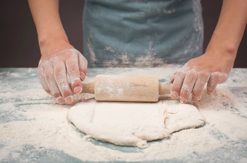 Baker rolls out dough for pizza, flatbread or pastry with rolling pin, prepare ingredients for