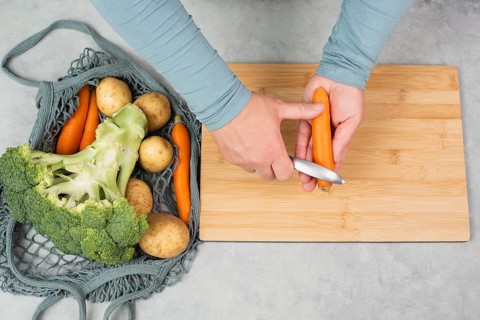 Peel carrot with scraper sharpener, prepare healthy food with vegetables, fresh organic nutrition,