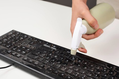 Cleaning computer keyboard in office, spraying water with a spray bottle dusty and dirty