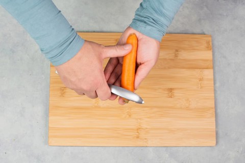 Peel carrots with scraper sharpener, prepare healthy food with vegetables, fresh organic nutrition,