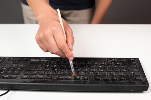 Cleaning computer keyboard in office with rubber protective glove and a brush, dusty and dirty