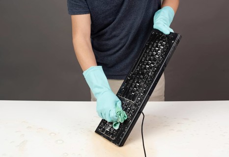 Cleaning computer keyboard in office with rubber protective glove, whiping with water and soap,