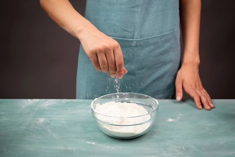 Baker sprinkles salt into a bowl with flour, prepare dough for artisan bread or pizza, ingredients