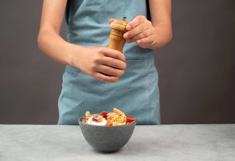 Putting pepper in a pasta salad, sliced mushroom, tomato, red pepper pieces and tuna, healthy food