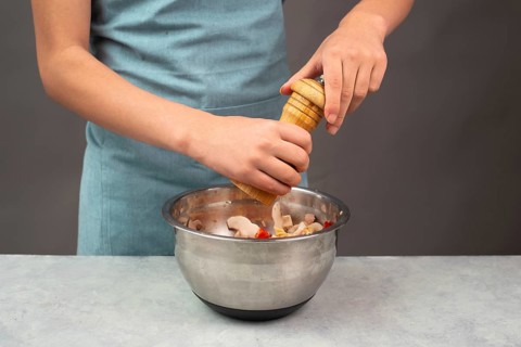 Putting pepper in a pasta salad, sliced mushroom, tomato, red pepper pieces and tuna, healthy food