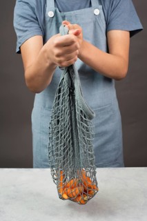 Holding fresh carrots in a reusable grocery mesh bag, vegetables from the market, healthy food and