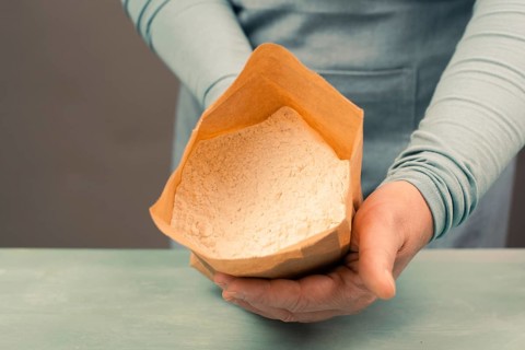 Baker holds paper bag with white wheat flour, baking ingredient for bread, pizza or pastry