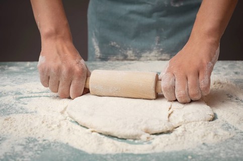 Baker rolls out dough for pizza, flatbread or pastry with rolling pin, prepare ingredients for
